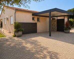 Ein modernes Haus mit überdachter Terrasse, einem Schotterweg und Kübelpflanzen.