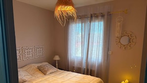 Quarto com cama, mesa de cabeceira, abajur, janela com cortinas e detalhes na parede.