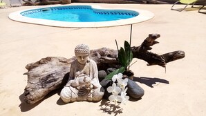 Área de piscina com estátua de Buda, pedras e orquídeas brancas.