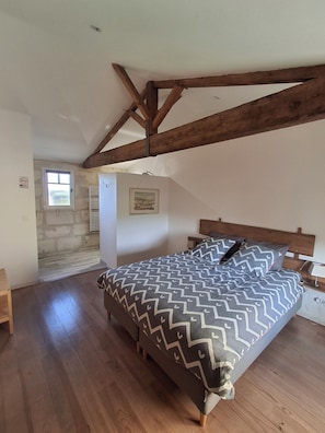 Een slaapkamer met een bed, houten balken, een stenen muur, een raam en een schilderij.