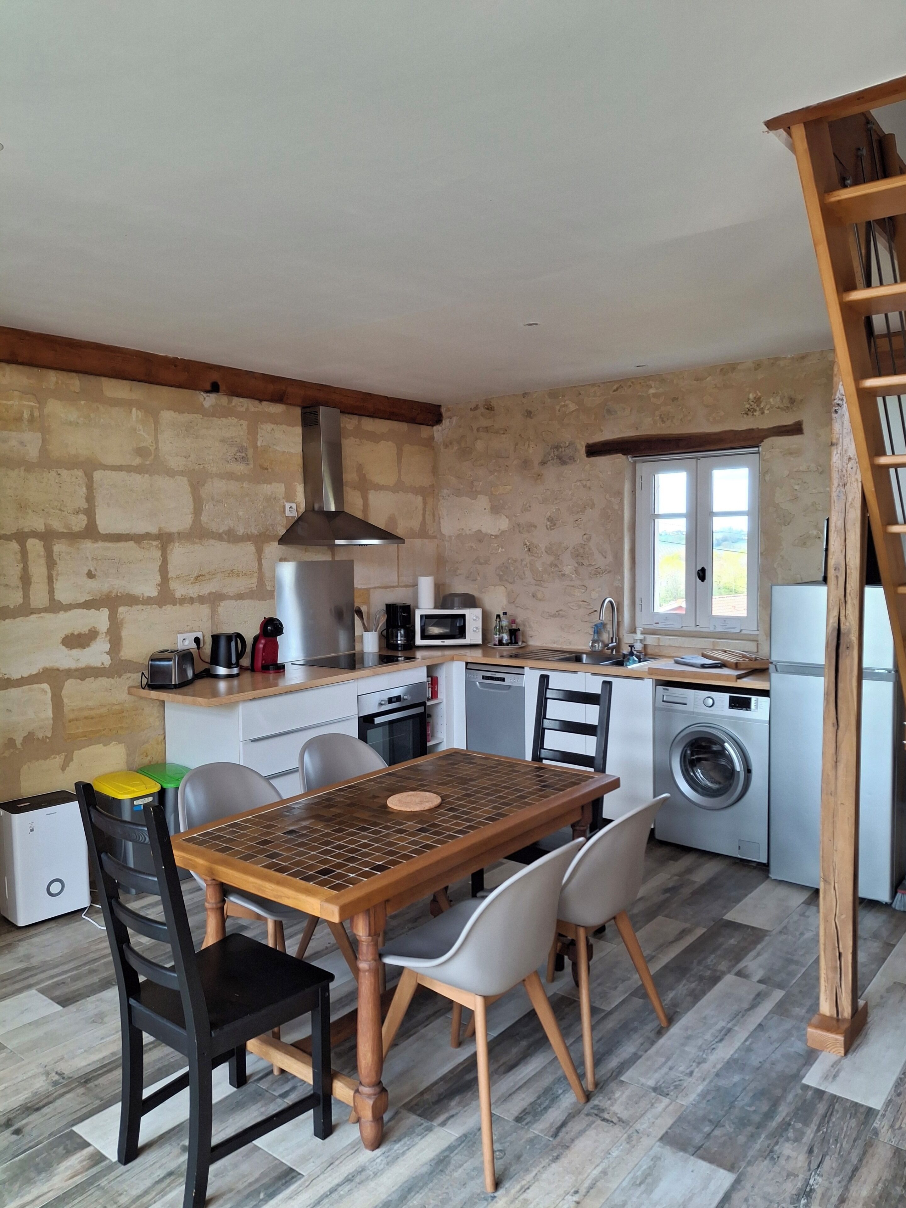 A compact kitchen with a dining table, chairs, a washing machine, and a wooden staircase.
