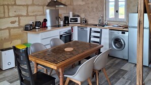 A compact kitchen with a dining table, chairs, a washing machine, and a wooden staircase.
