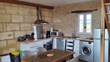 A compact kitchen with a dining table, chairs, a washing machine, and a wooden staircase.