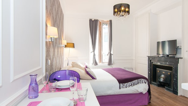 A hotel room with a bed, a television, a fireplace, and a dining area with a table set for two.
