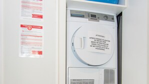 A compact laundry room with a washing machine and dryer, a blue laundry basket on top, and informational posters on the wall.