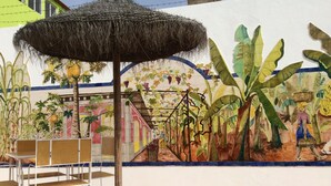 A mural of a tropical garden with a thatched umbrella and metal chairs in front. - Apartment for rent. on the island of Sao Vicenter Mindelo near the beach (Mindello)