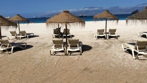 A beach with rows of white lounge chairs and thatched umbrellas, a clear blue sea, and distant mountains. - Apartment for rent. on the island of Sao Vicenter Mindelo near the beach (Mindello)