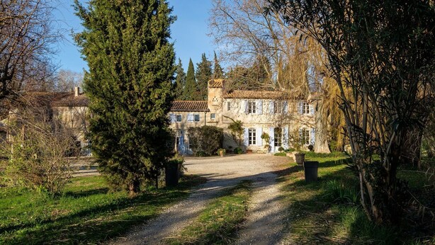 A historic stone building with a gravel driveway leading to a gated entrance.