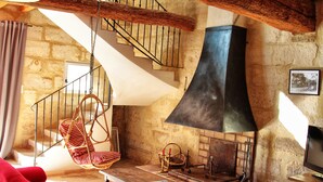 A cozy living room with a stone wall, a hanging chair, a fireplace, and a staircase.