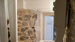 Ein schmaler Flur mit Steinwand, einer weißen Tür und einer kleinen Spüle.