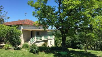 Une maison avec un toit recouvert de tuiles rouges, un balcon et un grand arbre au premier plan.