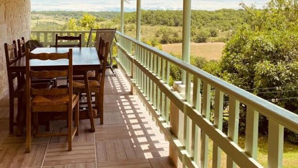 A covered outdoor area with a table and chairs, a railing, and a view of a green landscape. - white stone cottage in the countryside, with swimming pool. Magnificent view (PORTE-DU-QUERCY)