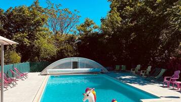 Une piscine avec un flotteur en forme de licorne, entourée de chaises longues et d’un espace abrité.