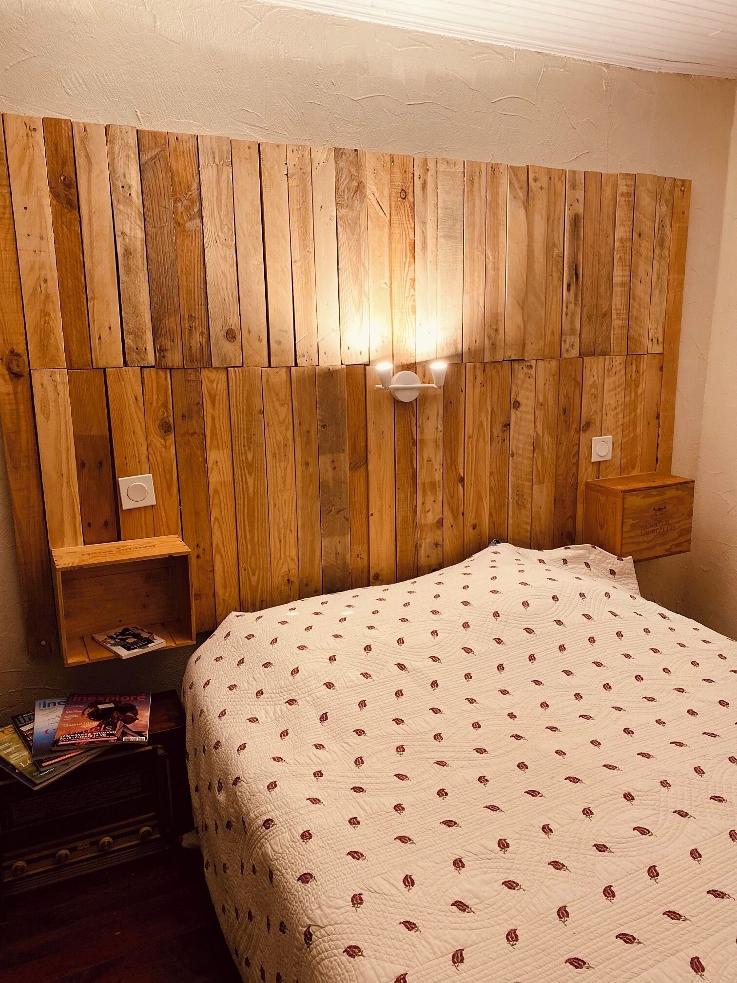 Une chambre à coucher avec une tête de lit en bois, une table de chevet et un lit recouvert d’une courtepointe à motifs.