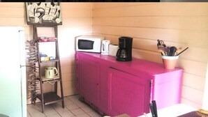 A kitchen with a stove, sink, and refrigerator. There is a shelf with kitchen utensils and a pink cabinet. - T2 INDIANA air-conditioned, DESHAIES 350 m Grande Anse, 2/3 people, large terrace.  (Deshaies)
