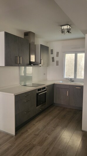 A modern kitchen with dark cabinetry, a built-in oven, and a window providing natural light. - Spacious 3-room apartment in the center of the village (Cauterets)