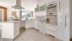 A modern kitchen with white cabinetry, a central island, a built-in oven, and a dishwasher. - 110 m² villa with a pool and breathtaking views, not overlooked. (La Motte)