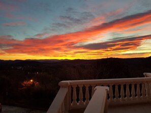 Un balcon doté d’une balustrade, d’où l’on peut admirer un coucher de soleil aux couleurs éclatantes dans le ciel.
