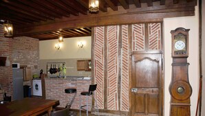 Une cuisine rustique avec des murs en briques apparentes, des poutres en bois et une grande porte en bois ornée d’une horloge.