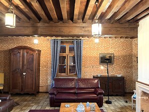A room with a wooden ceiling, brick walls, a leather sofa, a wooden cabinet, and a table with decorative items.