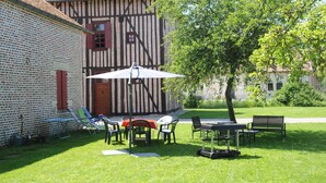Une cour avec une table et des chaises, un arbre, et un bâtiment dont la maçonnerie et la charpente sont apparentes.