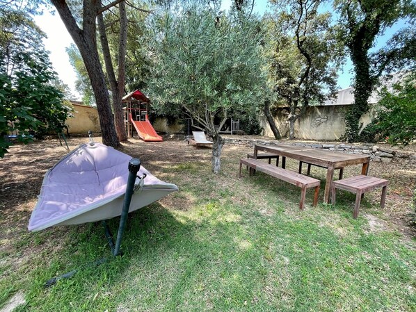Un cortile con tavolo da picnic, ombrellone e area giochi con uno scivolo.