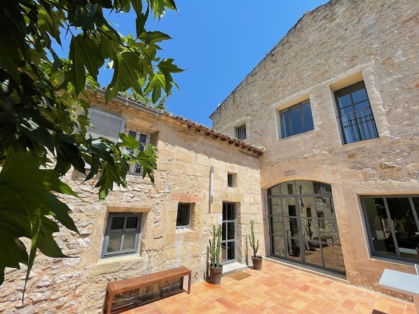 Un bâtiment en pierre doté d’un patio carrelé, de grandes fenêtres et de plantes en pot.