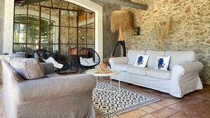 A cozy living room with a stone wall, a white sofa with decorative pillows, a grey armchair, and a patterned rug.