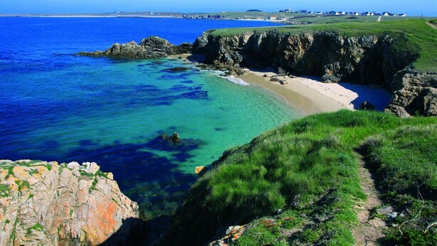 Un paysage côtier caractérisé par une eau d’un bleu limpide, une plage de sable et des falaises rocheuses.