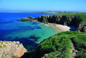 A coastal landscape with clear blue waters, a sandy beach, and rocky cliffs.