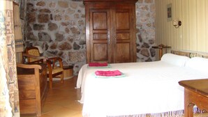 Une chambre avec un mur en pierre, une armoire en bois, un lit et une chaise.