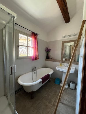 A bathroom with a bathtub, a shower, a sink, and a window with a curtain.