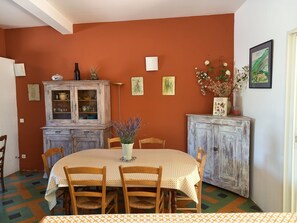 Uma sala de jantar com uma mesa redonda, cadeiras de madeira, um armário com portas de vidro e obras de arte penduradas na parede.