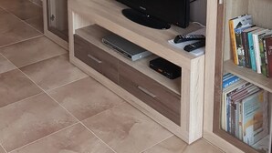 Una sala de estar con un televisor de pantalla plana sobre un soporte de madera, un aparador de vidrio con copas de vino y una estantería con libros.