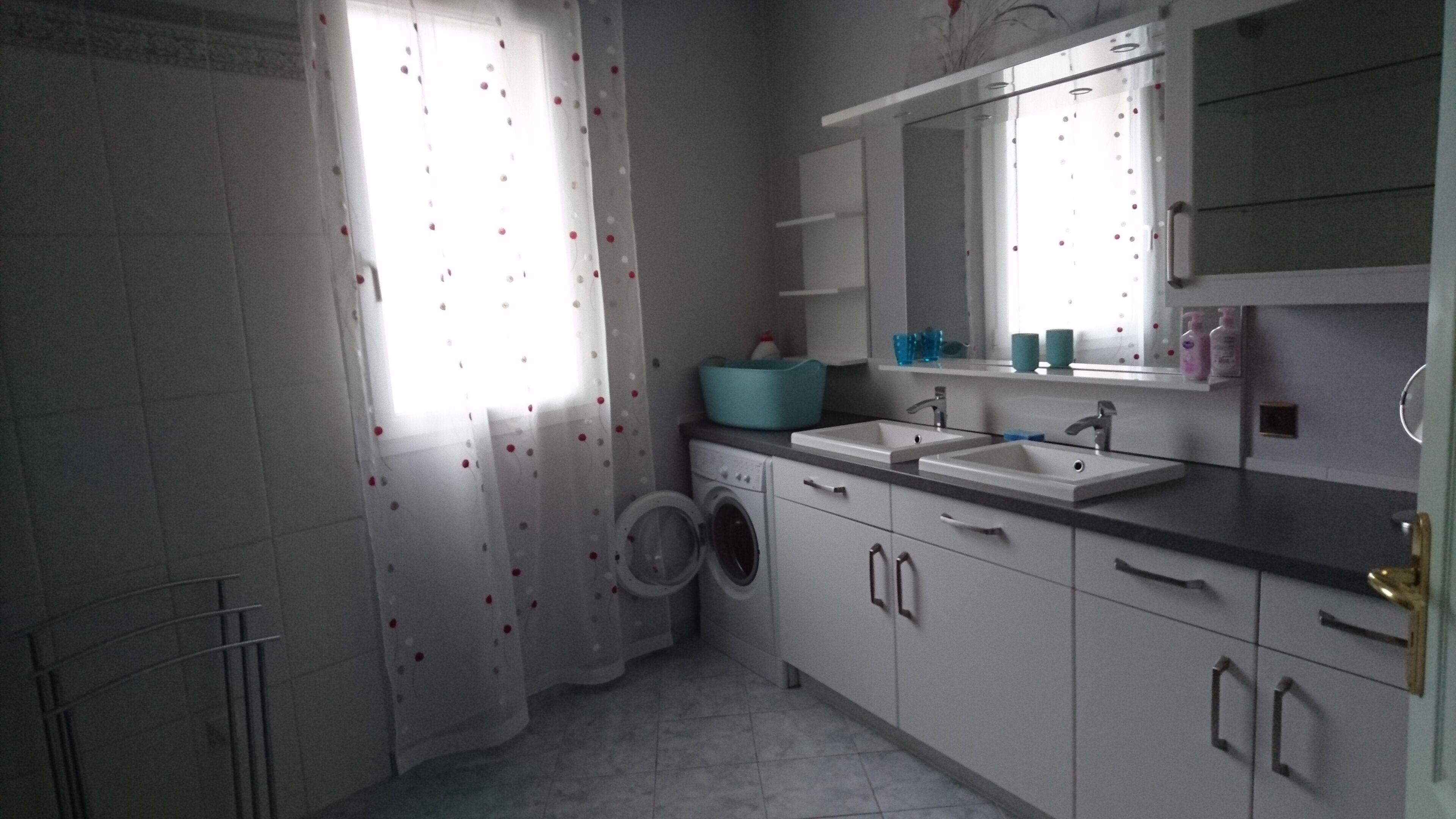 Un baño pequeño y funcional con lavadora, dos lavamanos y un espejo grande sobre el lavabo.