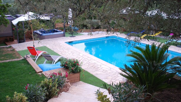 Un jardin avec une piscine, un jacuzzi et une terrasse en bois avec des chaises.
