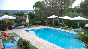 Une piscine entourée de verdure et dotée d’une terrasse en bois, avec des chaises longues et des parasols.