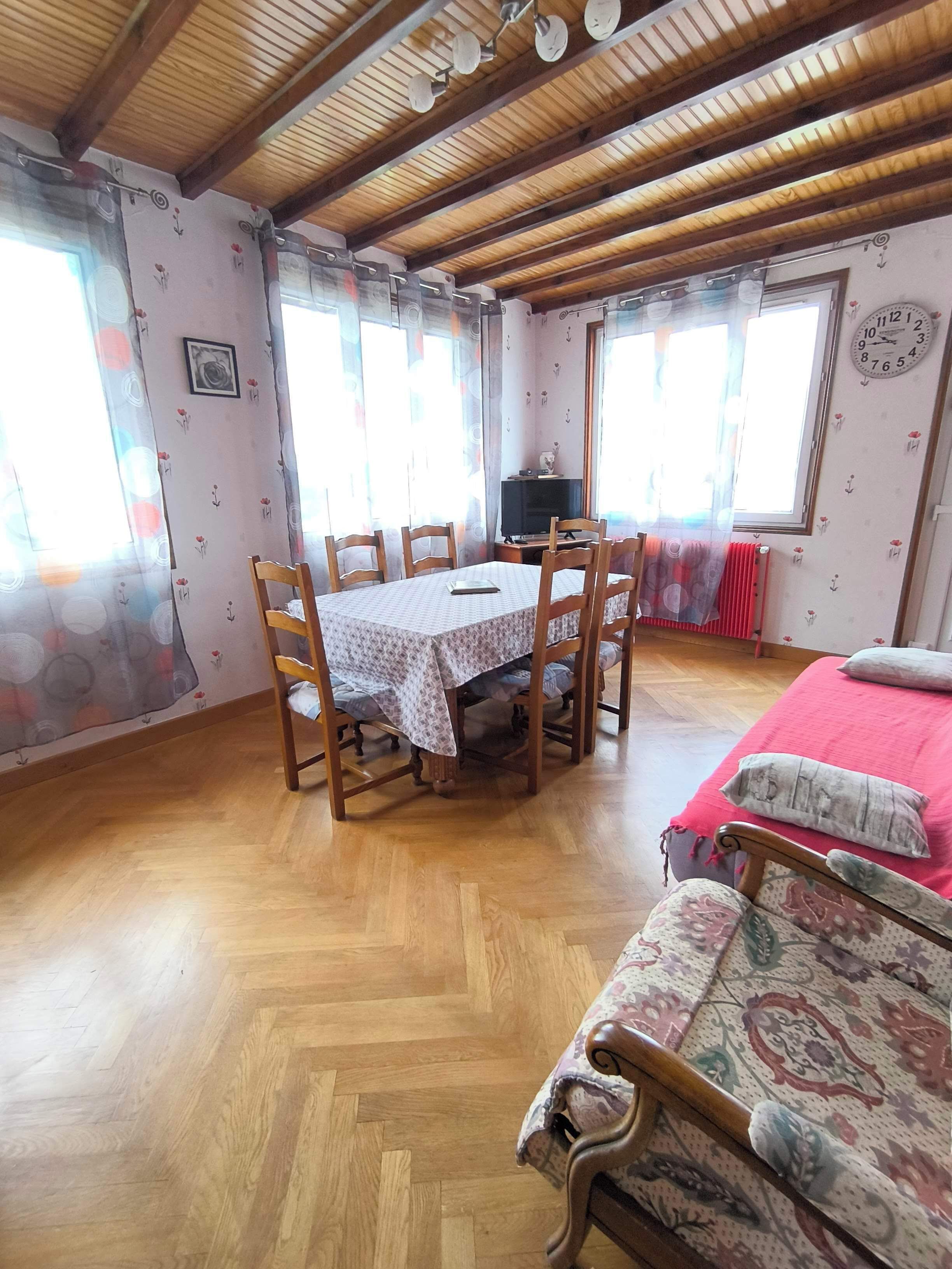 A cozy room with a wooden ceiling, a dining table with chairs, a TV, and a bed with a red blanket.