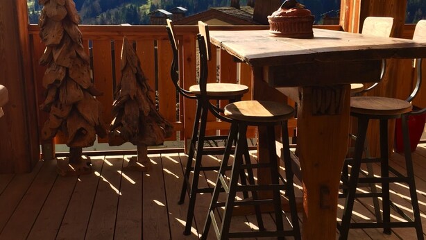 Une terrasse en bois avec une table et des chaises, offrant une vue sur un paysage montagneux.