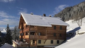 Un chalet en bois doté d’un balcon, entouré d’un paysage enneigé et de montagnes.