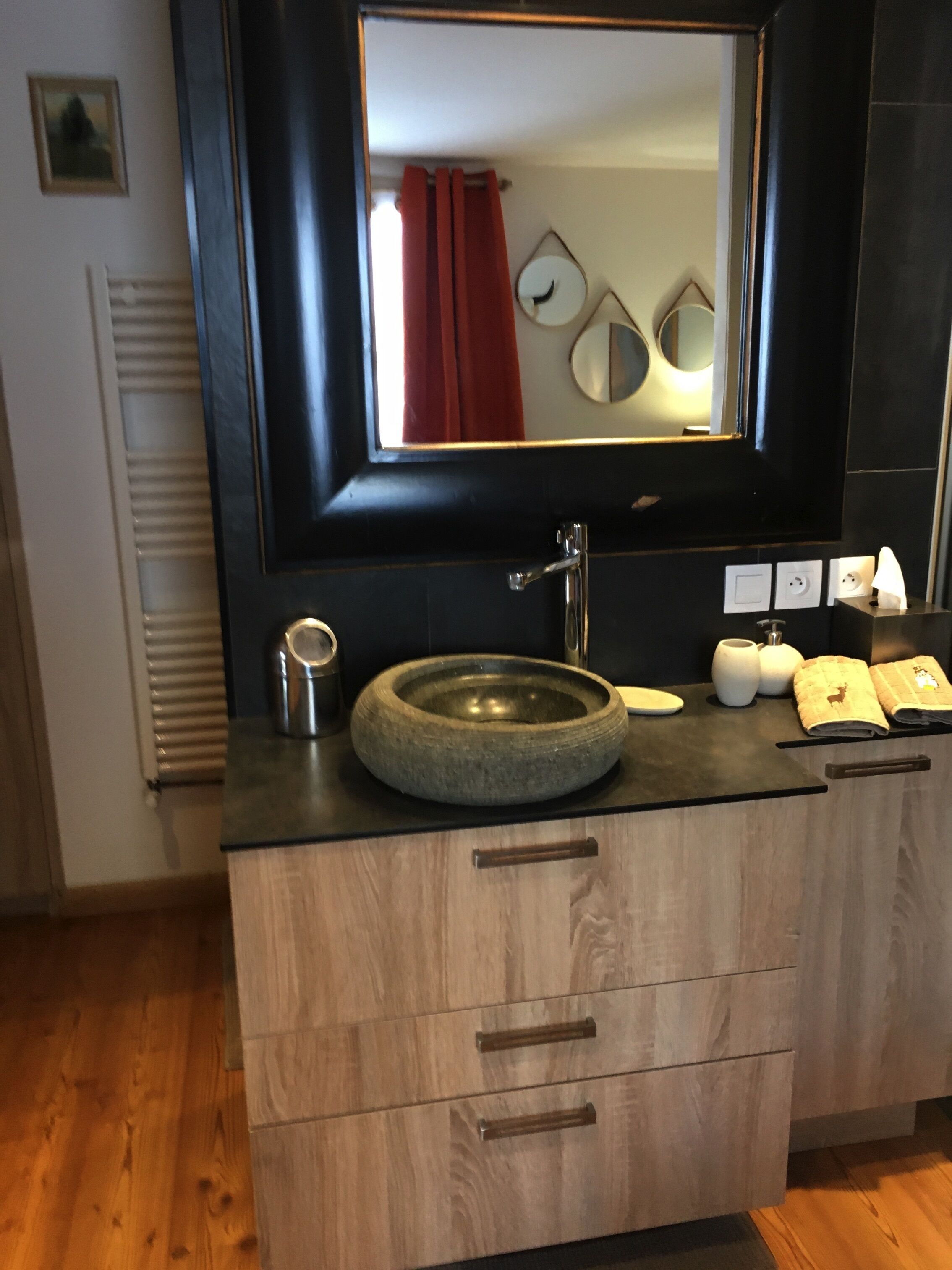 Een moderne badkamer met een stenen wasbak, houten kastjes en een grote spiegel.