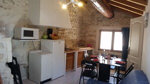 Cozinha compacta com parede de pedra, micro-ondas, pequena geladeira e área de refeições com mesa posta para dois.