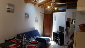 Uma sala de jantar com uma mesa posta para quatro pessoas, um sofá e uma televisão ao fundo.