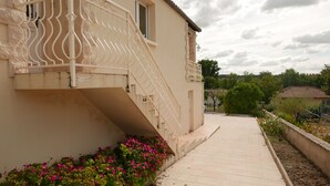 Un edificio beige con una scalinata che conduce a un balcone, circondato da un giardino fiorito di fiori rosa.