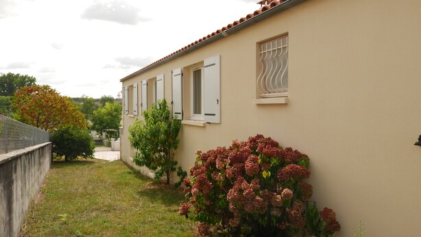 Un edificio con facciata beige, persiane bianche e una piccola finestra con grate bianche.