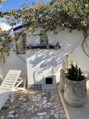 A courtyard with a mosaic-tiled floor, a white wall with a mosaic panel, a statue, and a cactus plant. - Dar Amandine Djerba midoun (Midoun Djerba)