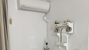 A white desk with a chair, an air conditioner, and a decorative shelf with small items. - Dar Amandine Djerba midoun (Midoun Djerba)