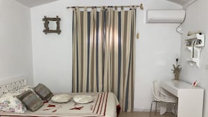 A bedroom with a bed, a desk, a chair, a curtain, and an air conditioning unit. - Dar Amandine Djerba midoun (Midoun Djerba)