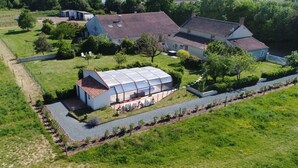 Een groot huis met een tuinkamer, omgeven door een omheind terrein met paarden.