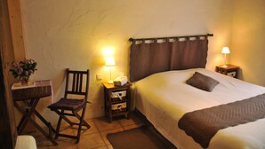 Een slaapkamer met een bed, een stoel, een nachtkastje, een lamp en een tafeltje met een bloevas.